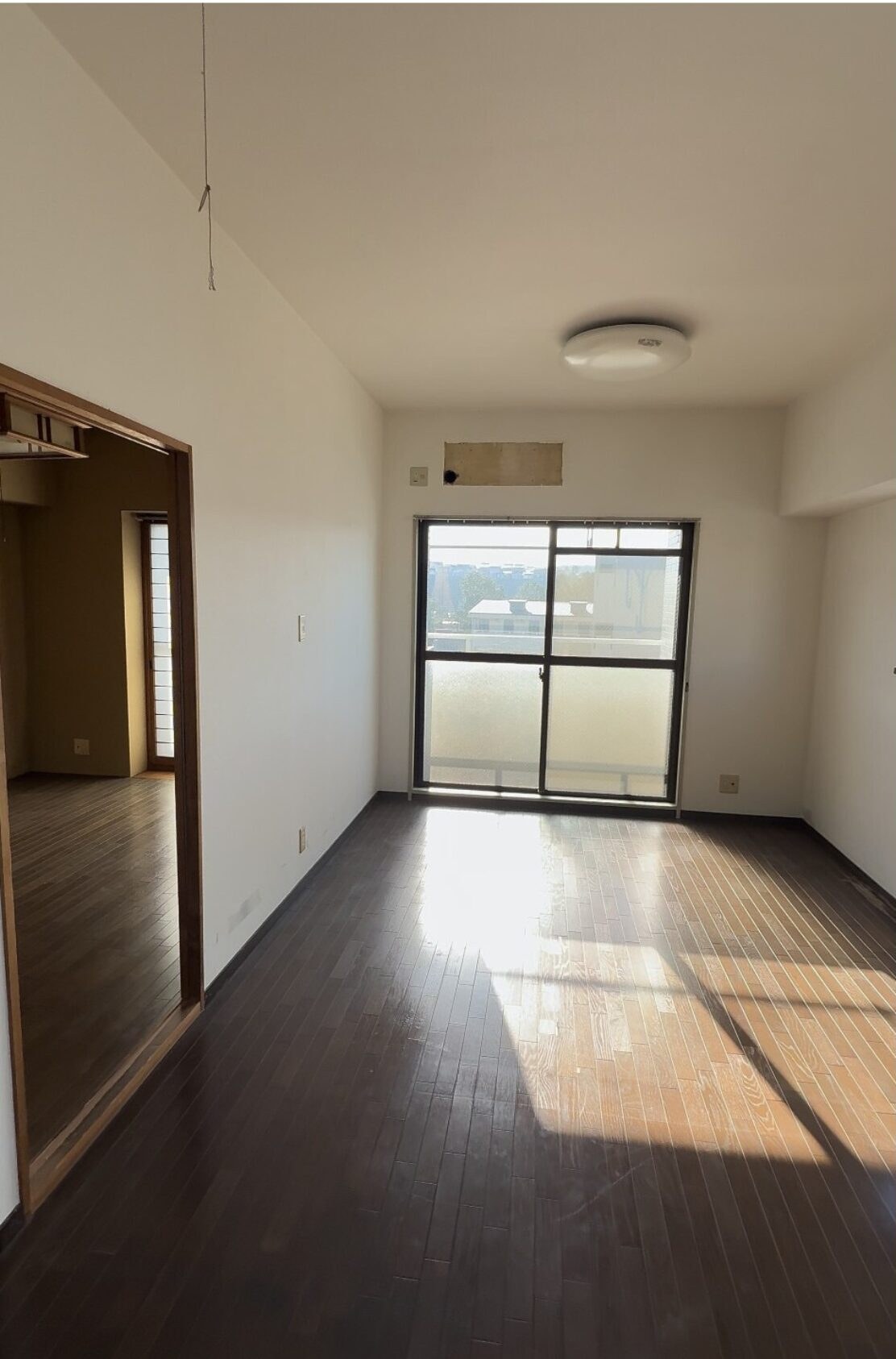 濃い色の床と古い照明があるマンションLDKの施工前